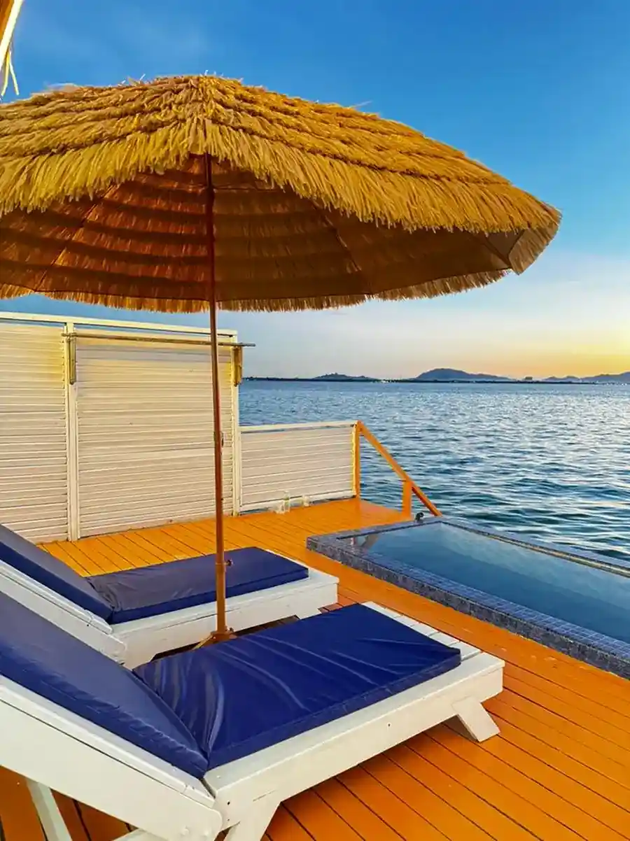 Relax on the private overwater balcony featuring comfortable blue sun loungers, a plunge pool, and a thatched umbrella at Danglai Resort, Semporna.