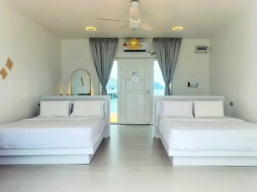 Clean and bright interior of a family water chalet at Danglai Resort Semporna showing two comfortable beds and a glass door leading to the sea view balcony.