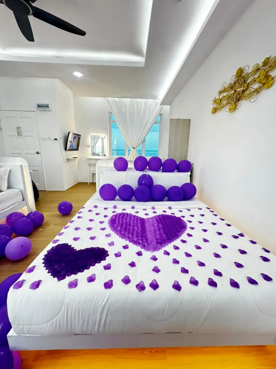 Close up of a romantic bed decoration featuring a large heart made of purple petals and balloons in a sea view suite at Danglai Resort Semporna.