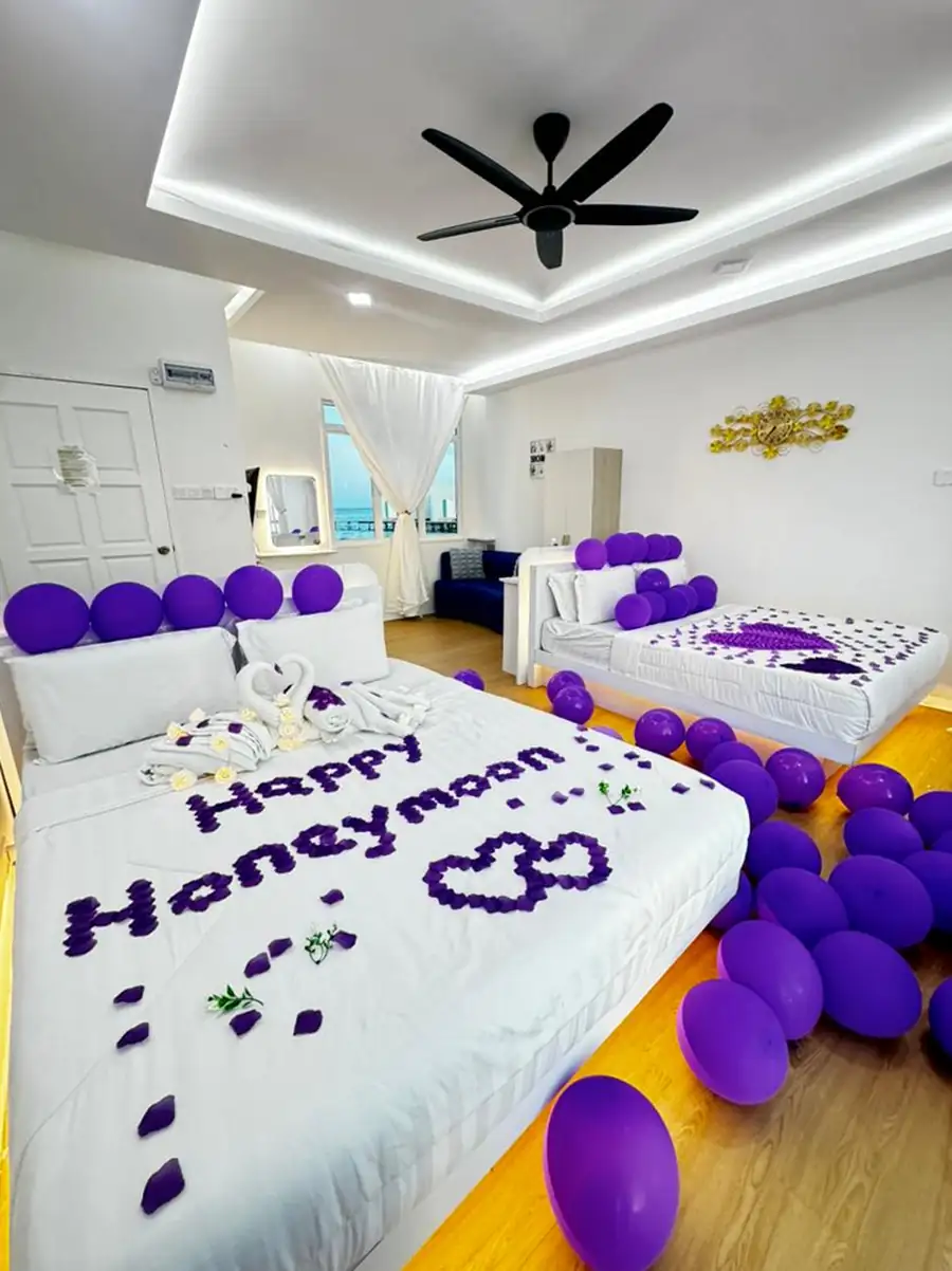 Romantic honeymoon suite setup at Danglai Resort Semporna decorated with purple balloons, towel swans, and flower petals spelling Happy Honeymoon on the bed.