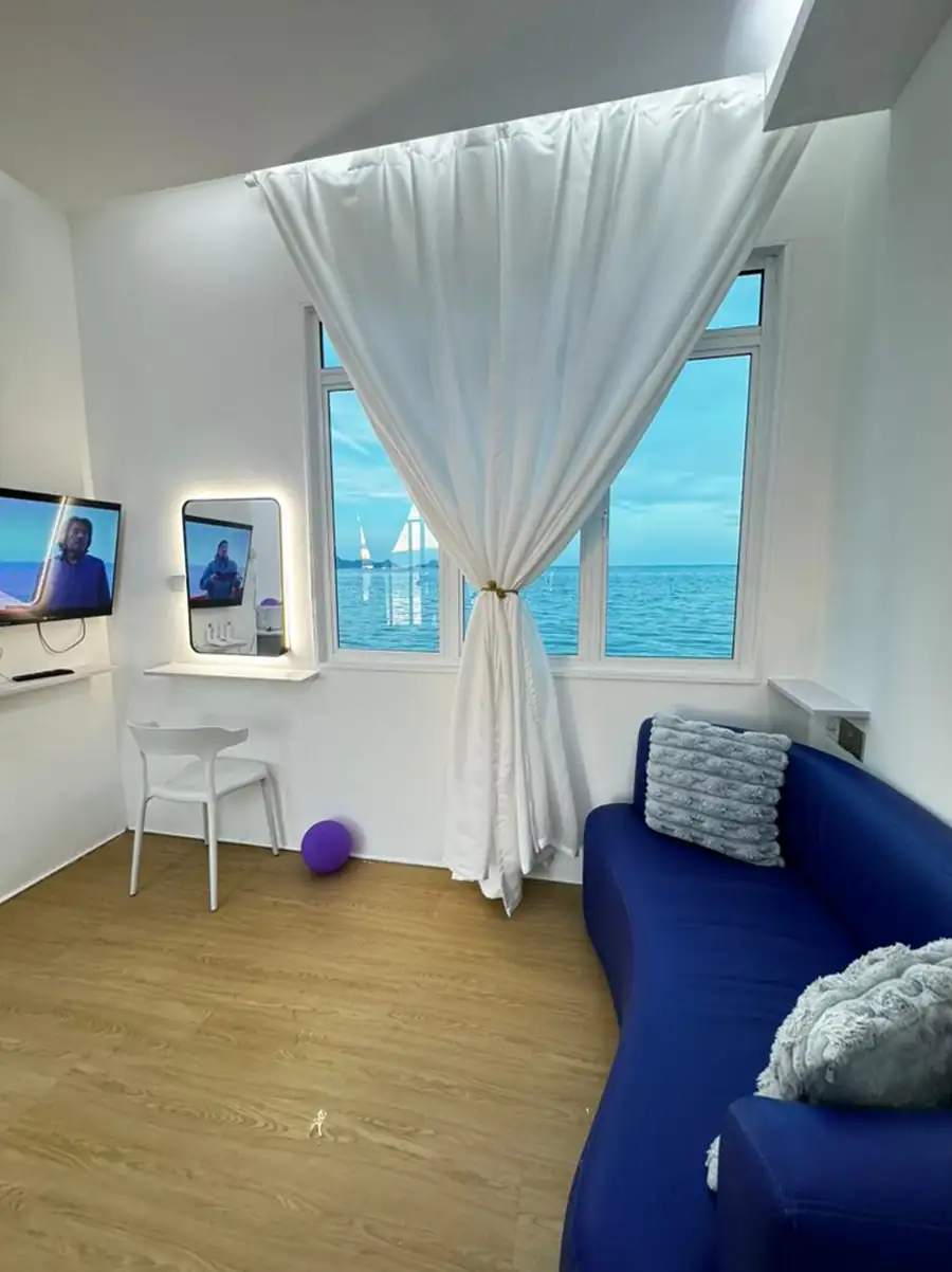 Cozy interior sitting area at Danglai Resort Semporna featuring a blue sofa, vanity desk, and a window framing a beautiful view of the ocean and passing boats.
