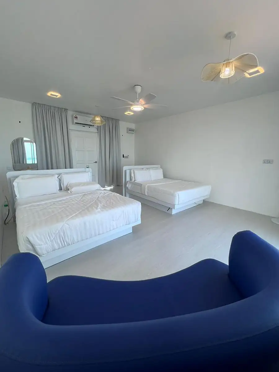 Wide interior view of a spacious suite at Danglai Resort Semporna featuring white beds, modern decor, and a unique blue curved sofa for relaxing.